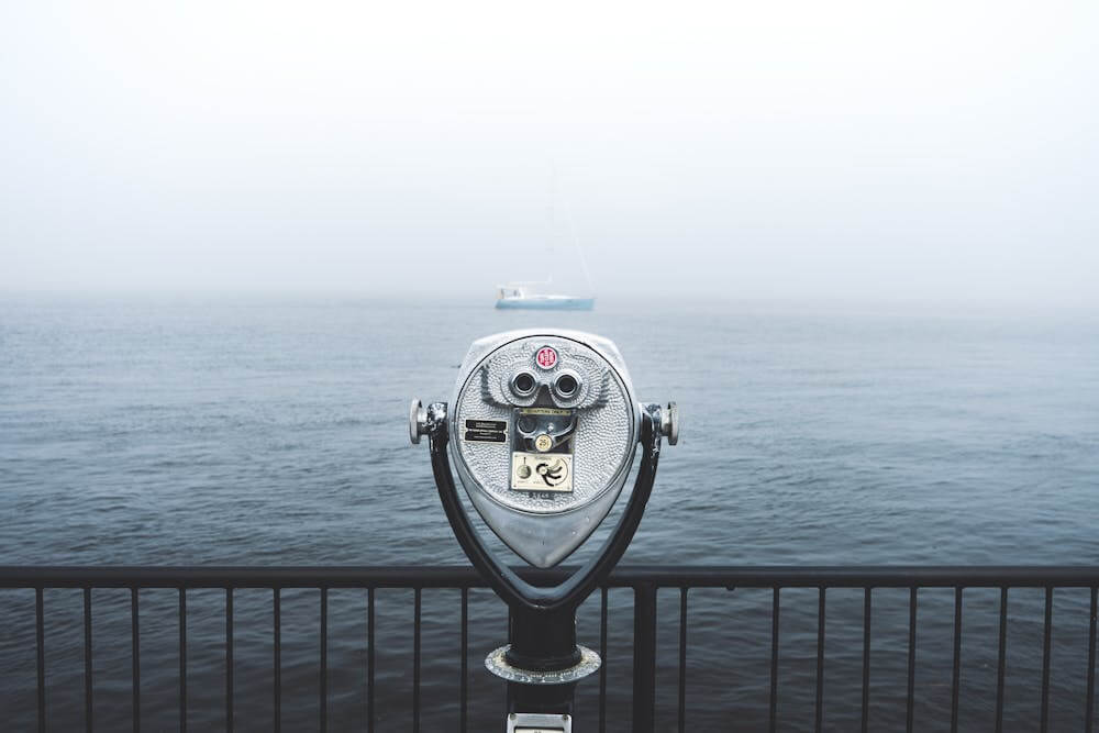 telescope by the pier overlooking the sea with a boat in the foggy background