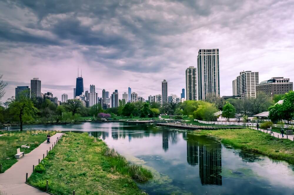 park with a pond benches and a cityscape in background